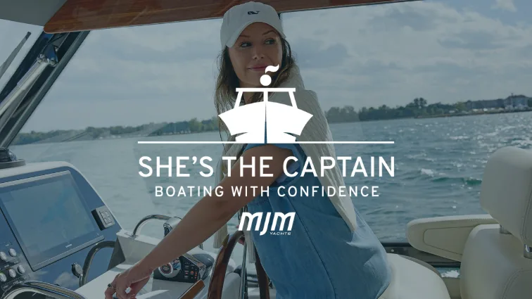 Woman at the helm of an MJM yacht under the She's the Captain, Boating with Confidence event banner.