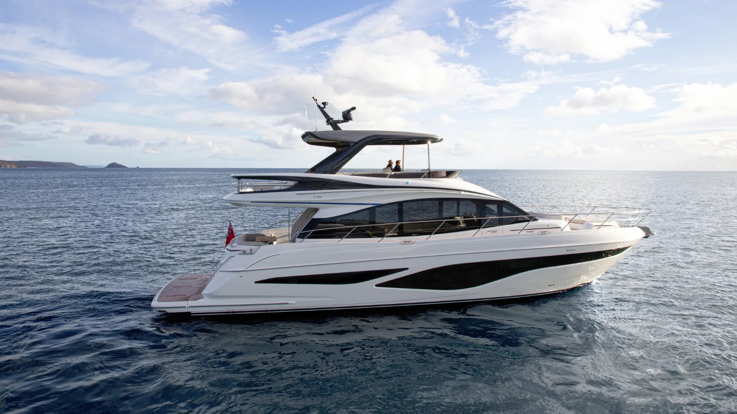 Princess F65 flybridge motor yacht resting on calm blue water, full profile view with islands behind.