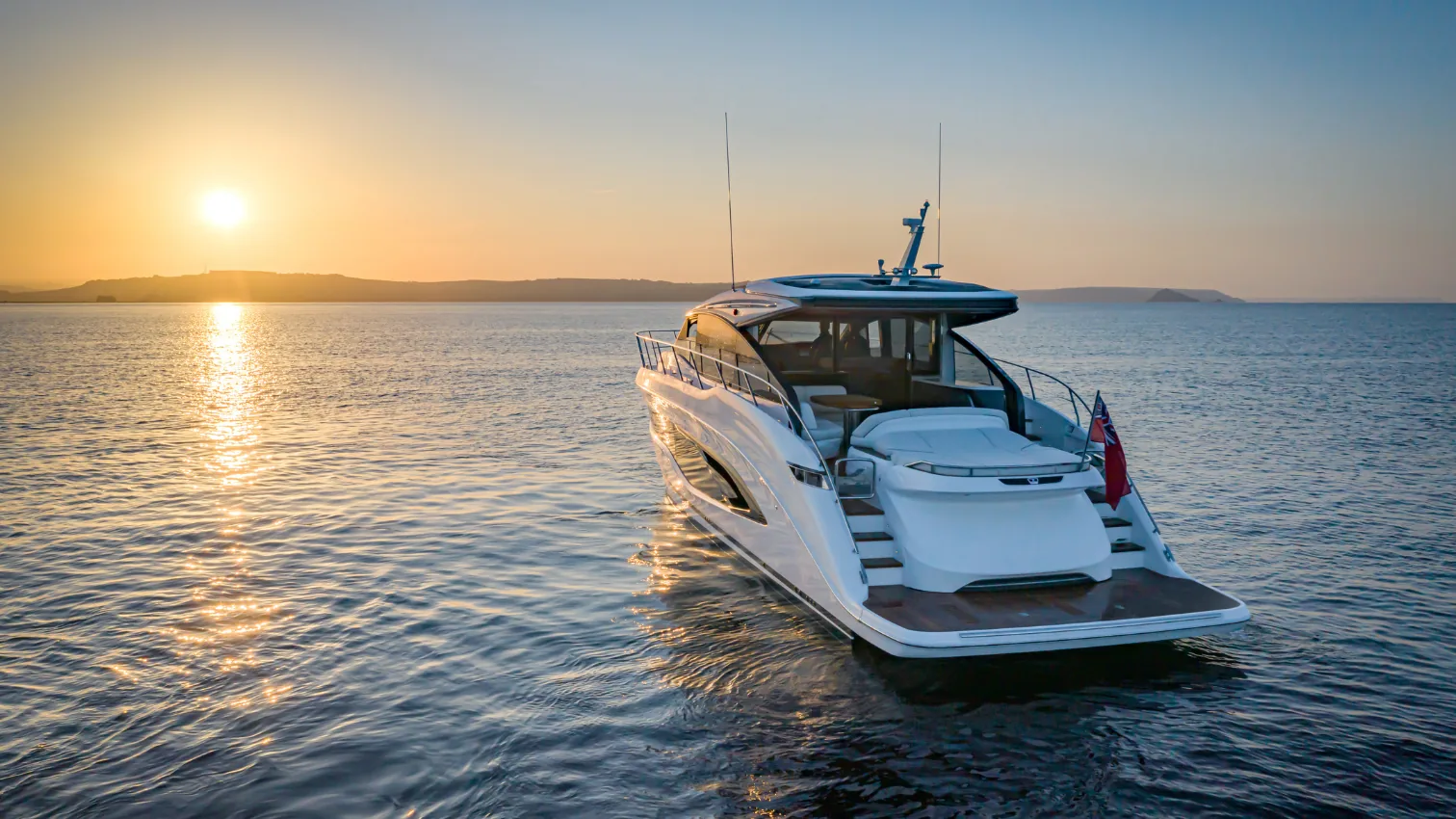 Princess V55 Sport yacht at anchor at sunset, stern quarter view with warm light over coastal hills.